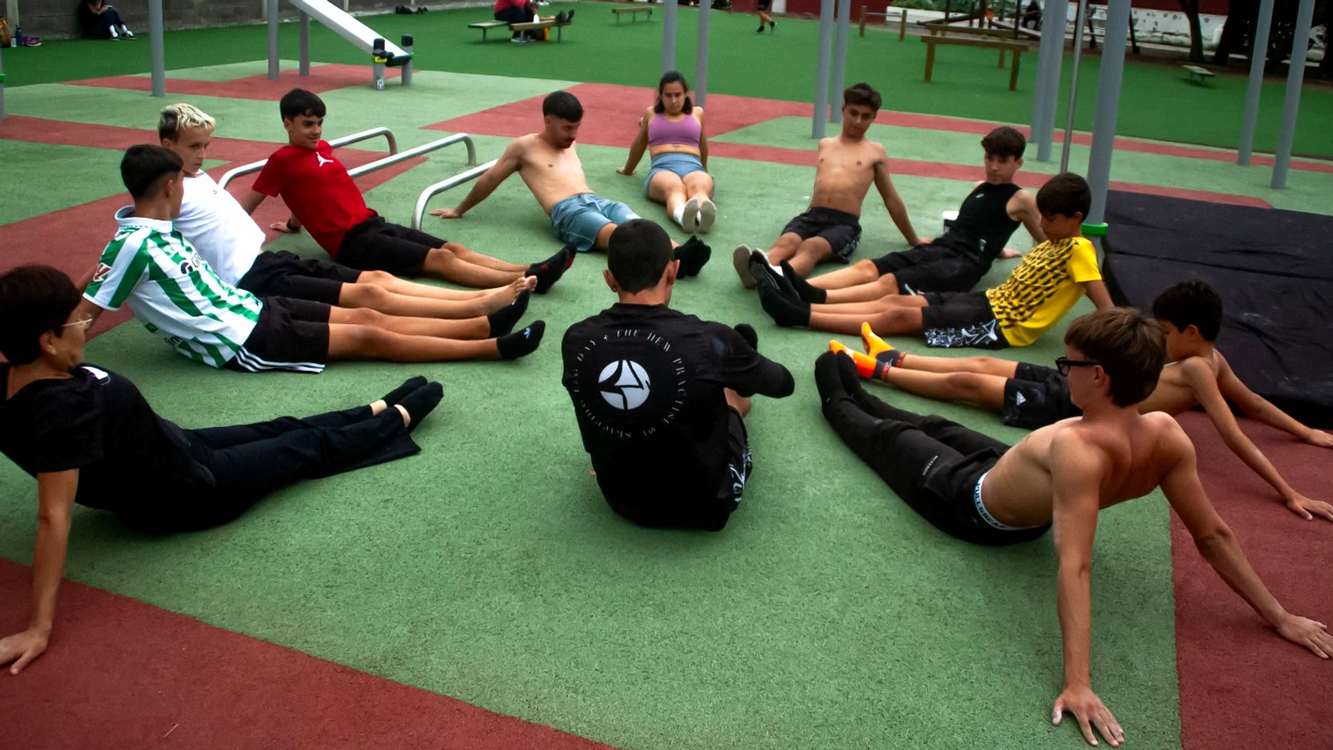 Grupo de alumnos de VoidSthenos sentados en círculo sobre el suelo del parque, estirando al final de una clase.