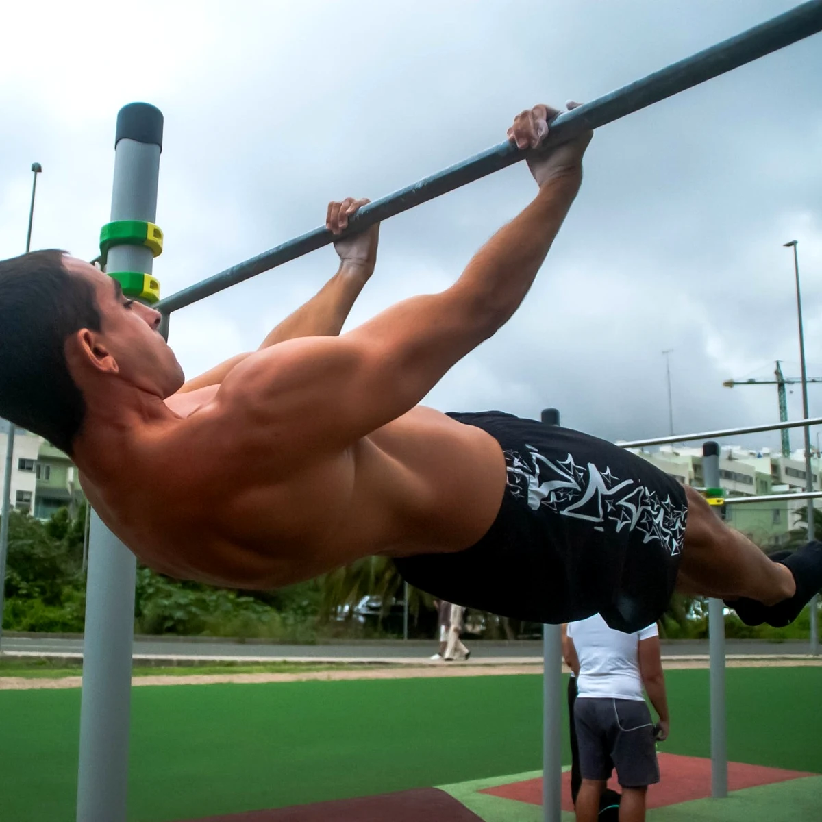 Un atleta de VoidSthenos sostiene un front lever, con el cuerpo recto y horizontal bajo la barra, en un parque de calistenia.